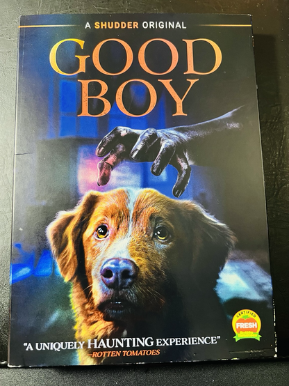 A photo of the front of the “Good Boy” DVD, showing a mysterious black hand reaching out towards the head of a medium sized brown and white dog. The dog looks towards the viewer unaware of the hand.